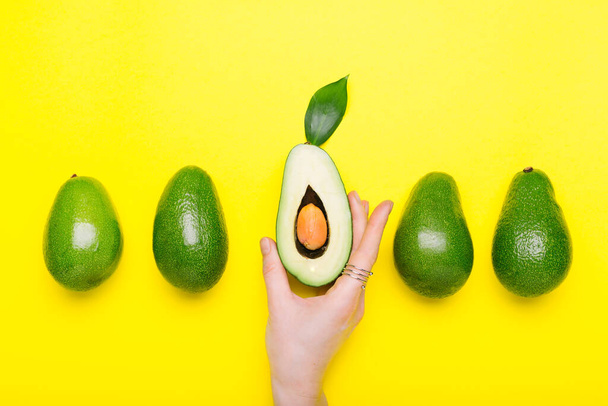 Fresh ripe organic green avocado in female hand with ring on color background, top view summer food concept. Minimal flat lay style avocados whole fruit on yellow background. - Fotografie, Obrázek