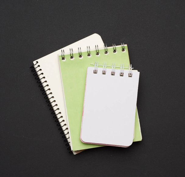 stapel van spiraal open notitieboekjes met blanco witte bladen op een zwarte achtergrond, bovenaanzicht - Foto, afbeelding