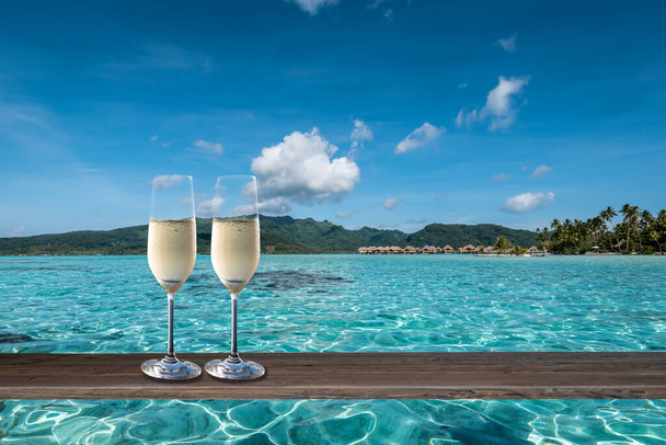 Celebración de vacaciones de verano de lujo con dos copas de champán en una mesa en la laguna de las Islas de la Sociedad. - Foto, imagen
