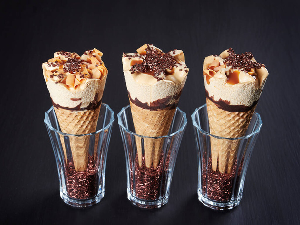 Tři karamelové zmrzlinové kornouty, zasazené do sklenic naplněných krystaly cukru, na tmavohnědém pozadí - Fotografie, Obrázek