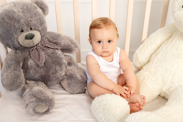 bebé niño de 1 año sentado en una cuna con grandes osos de peluche, bebé en el vivero - Foto, imagen