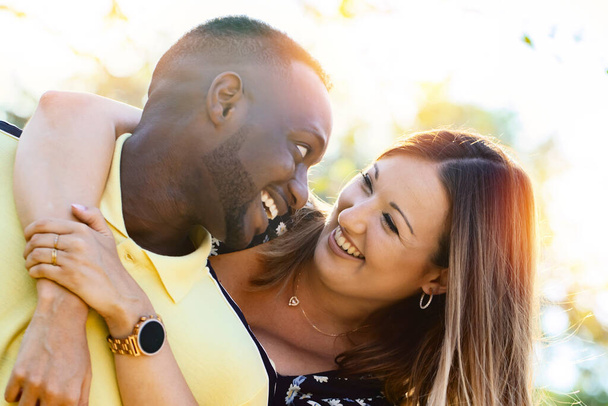 Nahaufnahme Außenporträt eines glücklichen multirassischen Paares. Junge kaukasische Frau umarmt schwarzen Freund lachend - Foto, Bild