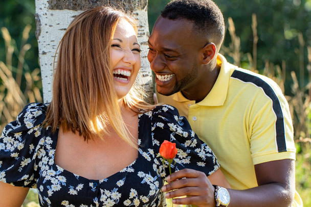 Nahaufnahme Porträt eines charmanten afrikanischen jungen Mannes, der seiner kaukasischen Freundin einen Blumenpark schenkt. Romantisches Paar lacht zusammen. - Foto, Bild