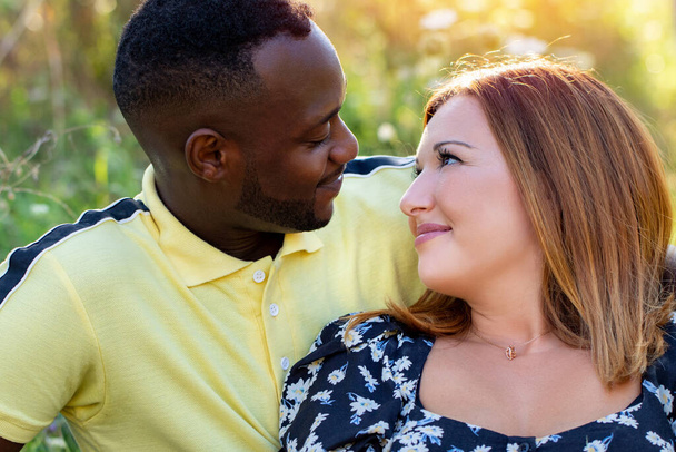 Close up venkovní hlava záběr multiracial mladý pár. Černošky muž a běloška žena při pohledu na sebe na pozadí přírody. - Fotografie, Obrázek