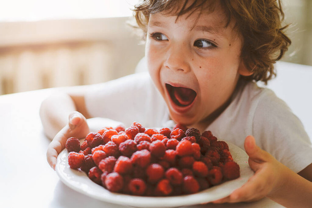 かわいい美しい男の子は新鮮なラズベリーを食べています。健康食品、小児期および発達.  - 写真・画像