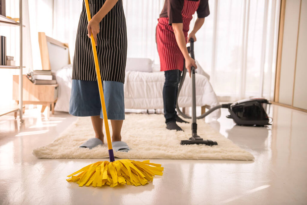 掃除機とモップを使って幸せなカップル家のベッドルームのカーペットと床をきれいにする。衛生と医療ライフスタイルの概念。週末の家事。新しい家やアパートに移動した後の洗浄. - 写真・画像