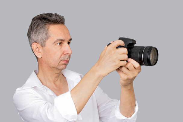 Portrait of handsome man in white shirt takes picture with camera. Isolated grey background - Fotografie, Obrázek
