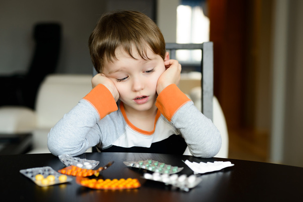 huolissaan 4-vuotias poika istuu pöydässä lääkkeiden kanssa
 - Valokuva, kuva