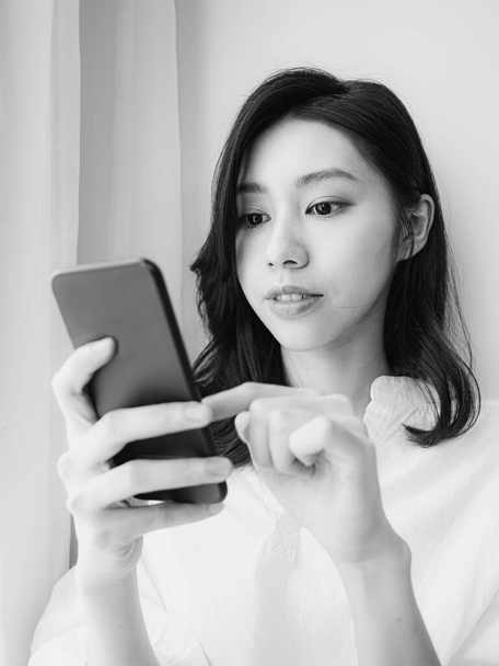 Jeune femme asiatique en utilisant smartphone à la maison en noir et blanc - Photo, image