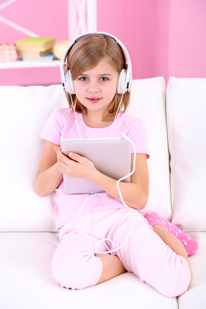 Little girl listening music sitting on sofa in room - Photo, Image