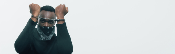 panoramic shot of handcuffed african american man looking at camera isolated on white, racism concept  - Photo, Image