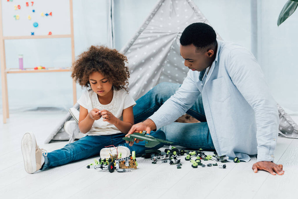 Африканский американский отец и ребенок, сидящие на полу и играющие с пластиковыми игрушками  - Фото, изображение