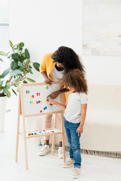 african american mother and daughter pointing with fingers at magnets on whiteboard  - Photo, Image