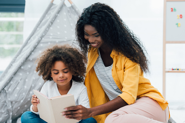 brunette african american mother and daughter reading book  - Zdjęcie, obraz
