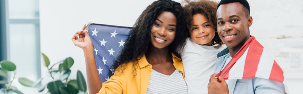 horizontal crop of african american family covered with flag of america looking at camera  - Valokuva, kuva