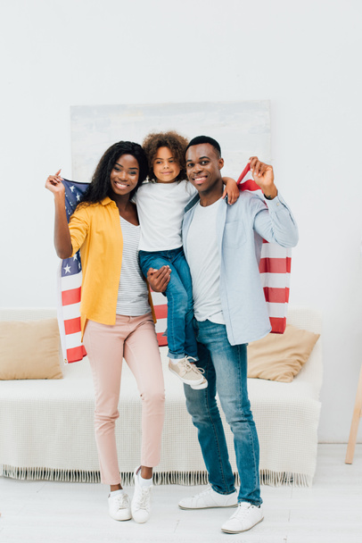 africano americano padre holding en armas niño y bandera de america cerca esposa - Foto, imagen