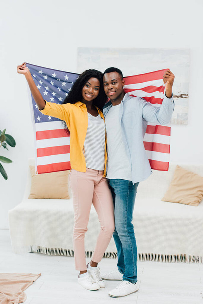 african american couple holding flag of america while standing at home  - Foto, Imagen