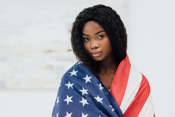 Африканская американка, покрытая флагом Америки, смотрит в камеру - Фото, изображение