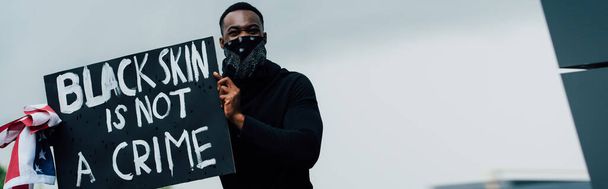 coltura orizzontale di uomo afro-americano che tiene cartello con la pelle nera non è un crimine lettering e bandiera d'America  - Foto, immagini