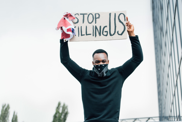 african american man holding flag of america and placard with stop killing us lettering outside  - Foto, imagen