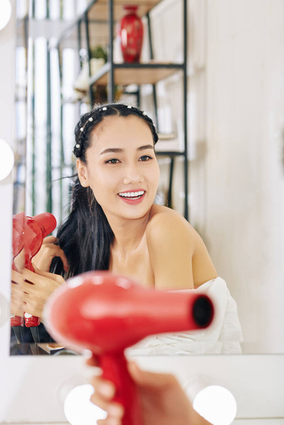 feliz hermosa joven asiática mujer soplando fuera cabello al prepararse en su vanidad - Foto, Imagen