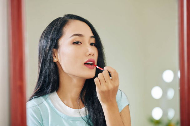 Atractiva joven vietnamita que abre la boca al aplicar lápiz labial líquido rojo - Foto, imagen
