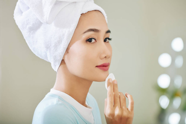 Jolie jeune femme vietnamienne appliquant du toner sur sa peau après avoir lavé le visage - Photo, image