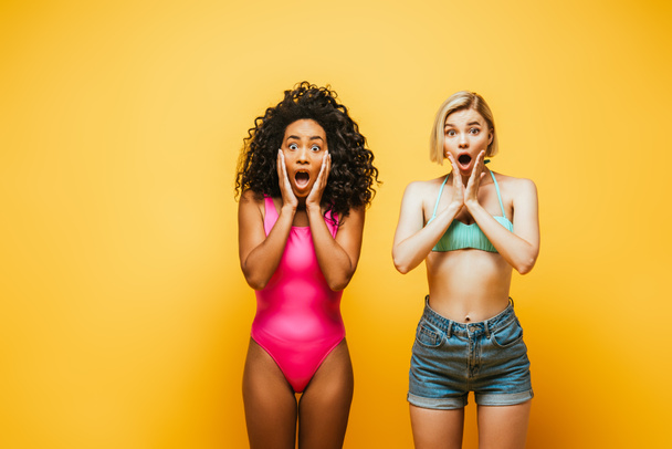 shocked multicultural women in summer outfit touching faces on yellow - Fotoğraf, Görsel