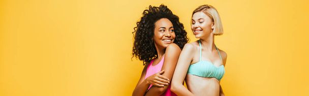 horizontal image of young african american woman standing back to back with blonde friend isolated on yellow - Foto, immagini