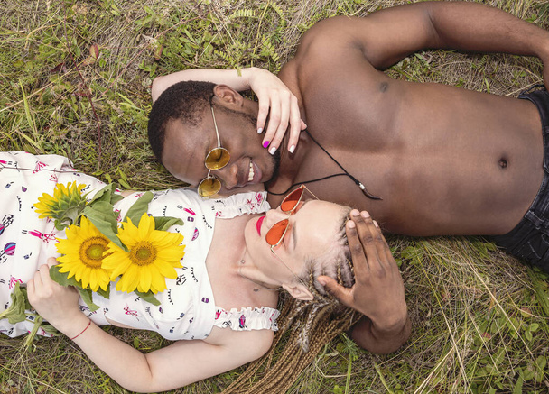 Um jovem casal de pessoas apaixonadas jazem na grama e olham um para o outro. Uma menina segurando um buquê de girassóis em suas mãos
 - Foto, Imagem