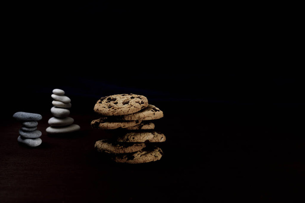 Vista frontal de Zen Pila de galletas de chocolate con una pila de piedras en la parte posterior y fondo oscuro - Foto, Imagen