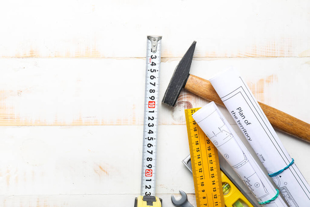 Measuring tape with builder's supplies and blueprints on wooden background - Фото, зображення