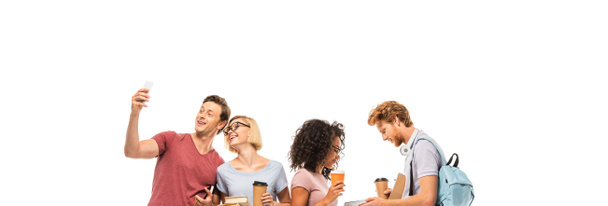 Panoramic shot of multiethnic students taking selfie and holding books with coffee to go isolated on white - Photo, Image