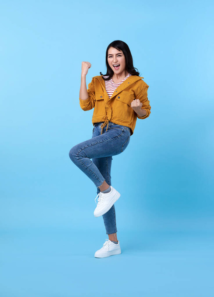 Happy asian woman in yellow shirt having fun and looking at the camera over blue background. - Φωτογραφία, εικόνα