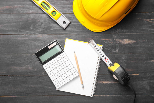 Measuring tape with builder's supplies, calculator and notebook on wooden background - Photo, Image