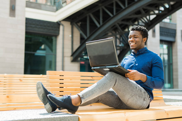 handsome young african man on bench with laptop - Fotó, kép