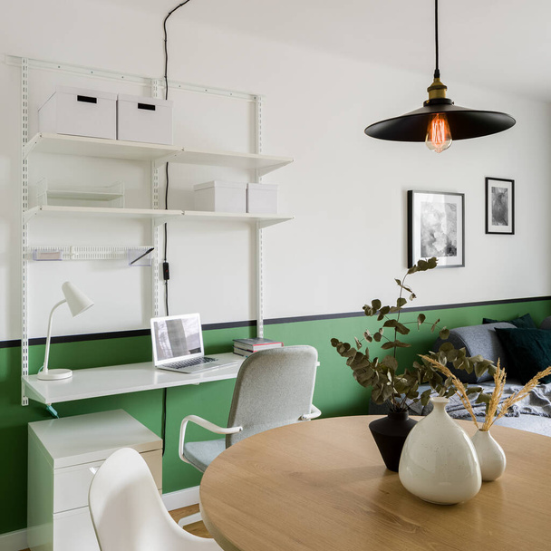 White industrial style home office area in living room with green wall and big wooden dining table - 写真・画像