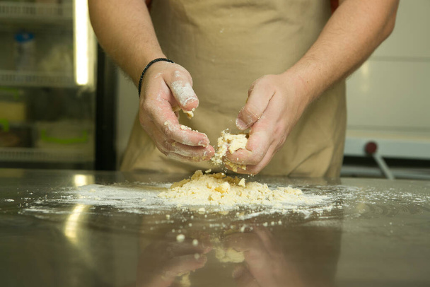 Η διαδικασία παραγωγής γλυκών αρτοσκευασμάτων με φρούτα. Ο σεφ φτιάχνει τη ζύμη με το χέρι. Ο άνθρωπος προσθέτει και αναμιγνύει τα συστατικά. - Φωτογραφία, εικόνα