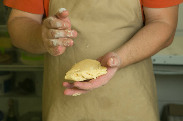 Η διαδικασία παραγωγής γλυκών αρτοσκευασμάτων με φρούτα. Ο σεφ φτιάχνει τη ζύμη με το χέρι. Ο άνθρωπος προσθέτει και αναμιγνύει τα συστατικά. - Φωτογραφία, εικόνα