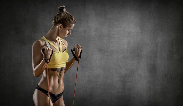 portrait young fitness woman performs exercise on grey wall background with empty space for text, gym concept - Photo, Image