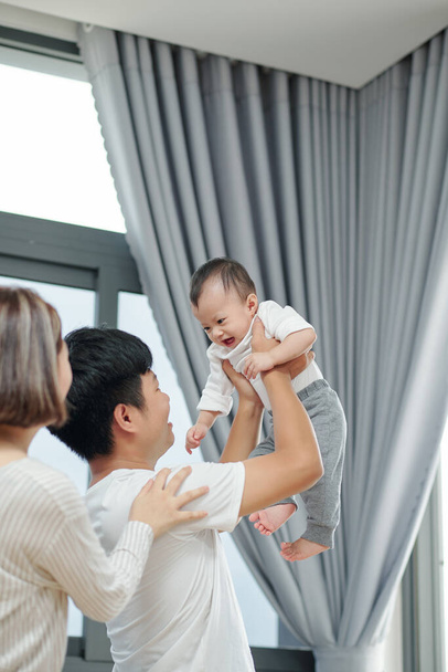 Heureux jeune père soulevant son nouveau-né quand sa femme se tient derrière - Photo, image
