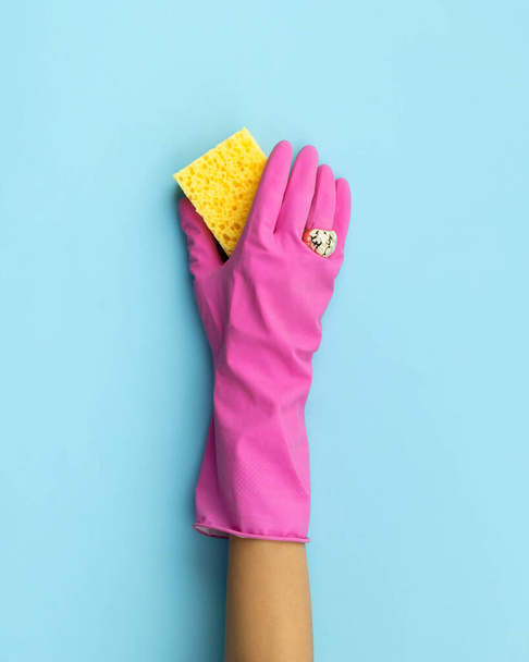 Ženská ruka v růžové gumové rukavici mytí houba modré pozadí. Úklid nebo úklid kreativní uspořádání. - Fotografie, Obrázek