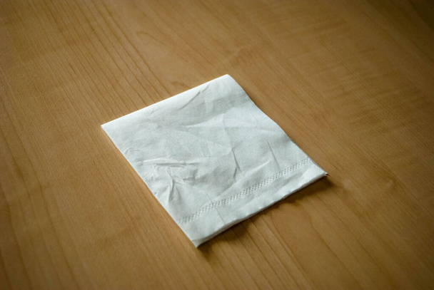 The image of paper tissue folded in a square lying on the table. White napkin folded in a square. - Photo, Image