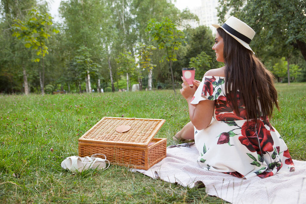Rear view shot of a stylish elegant woman sitting on the grass on a picnic, enjoying coffee - Valokuva, kuva
