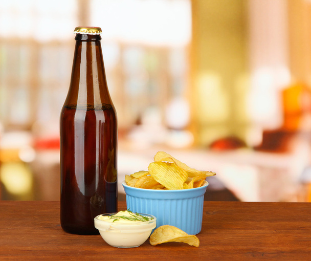 Potato chips and glass bottle with beverage, on bright background - Фото, изображение