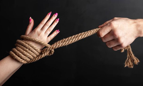 woman hands tied with a coarse rope close-up black background - Фото, изображение