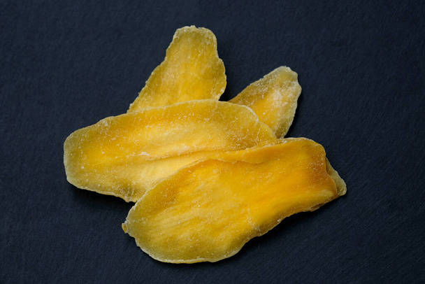 Mango seco sin azúcar. Pétalos de mango natural en una vista superior de tablero negro. Pulpa de mango seca, frutas secas, bocadillos vegetarianos saludables. - Foto, Imagen
