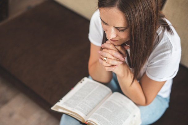 jonge vrouw bidden met bijbel relatie met God thuis - Foto, afbeelding