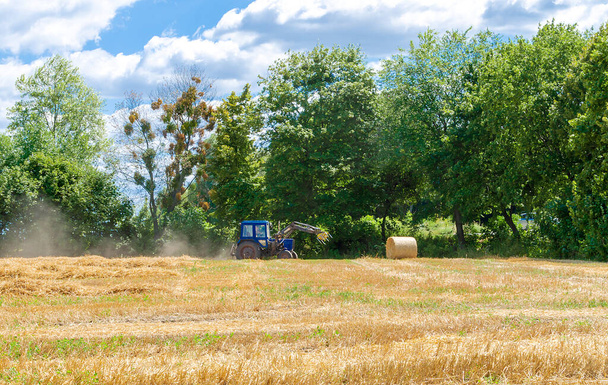 sláma v kulatých balících a traktor na poli, zemědělské práce v letní den - Fotografie, Obrázek