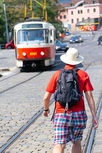 Touriste avec t-shirt rouge et chapeau blanc de l'arrière marchant dans la rue principale vers le tramway public. Prague. Voyages et promenades en République tchèque. - Photo, image
